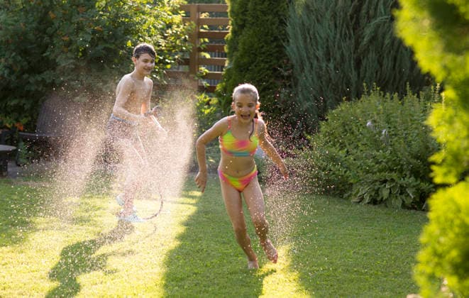 Glückliche Geschwister, die im Garten mit dem Gartenschlauch spielen und sich im sonnigen Hinterhof am Wasserspritzen erfreuen. Sommerzeit. Happy children brother and sister playing in the garden hose and having fun with spray of water in sunny backyard. Summer time. (License=RF) ,model released, Symbolfoto Copyright: xZoonar.com UliaxZotaninax 25041655 ,model released, Symbolfoto ,property released