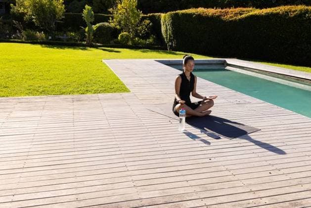 Asian female meditating on yoga mat at wooden pool deck, shorts, bottle, phone, copy space, model released, property released, 10.04.2025 06:00:00, 11794285 Copyright: xIMS-260310xcreatorid:x166x 11794285