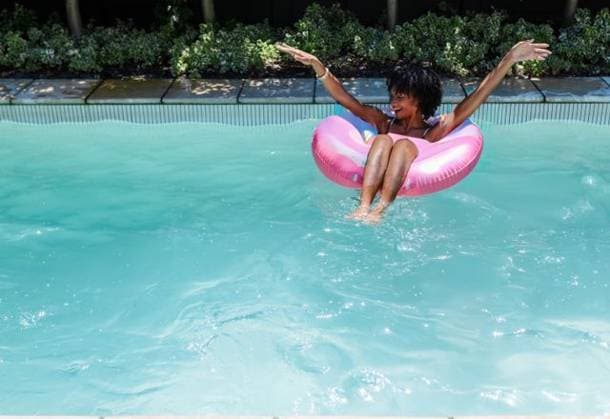 African American woman floating on pink donut float in blue pool wearing bikini, copy space, model released, property released, 26.02.2025 06:00:00, 13157771 Copyright: xIMS-260421_3xcreatorid:x166x 13157771