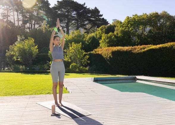 Indian woman practicing yoga in sportswear on wooden deck beside pool with mat, bottle, smartphone, model released, property released, 10.04.2025 06:00:00, 13157950 Copyright: xIMS-260421_4xcreatorid:x166x 13157950