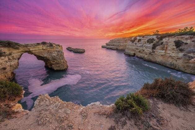 Dramatischer Blick auf den Sonnenuntergang von Arco de Albandeira am Praia de Albandeira an der Algarve, Portugal, mit rosafarbenem Himmel, Kalkstein Meeresbogen, Atlantikwasser und Dämmerungsfarben, die sich über der Bucht niederlassen Dramatic sunset view of Arco de Albandeira at Praia de Albandeira in Algarve, Portugal, with pink sky, limestone sea arch, Atlantic water, and twilight color settling over the cove Copyright: imageBROKER DmitryxRukhlenko ibxdmr17676943.jpg