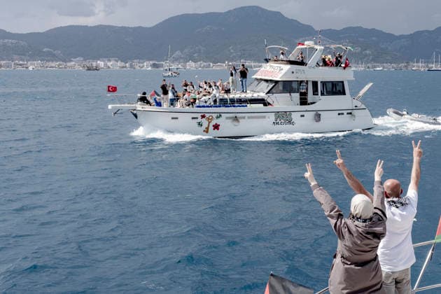 Global Sumud Flotilla Departure Marmaris Port Turkey People raise V-signs from a boat decorated with Palestinian flags as another vessel displaying solidarity signs sails past near the port in Marmaris, Turkey, on May 14, 2026. The Global Sumud Flotilla, carrying international activists and journalists, aims to sail across the Mediterranean Sea to Gaza to challenge the ongoing blockade and draw attention to the humanitarian crisis in the Palestinian territory. Marmaris Mugla Turkey Copyright: xMuratxKocabasx