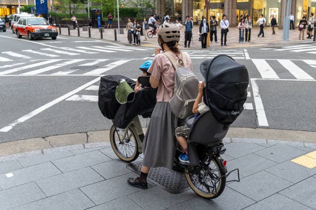 Fukuoka, Japan May 21, 2026: In Japan, a mother safely transports her children through urban traffic on a cargo bike. The image symbolizes sustainable mobility, everyday family life, cycling culture, and modern urban development. *** Eine Mutter transportiert in Japan Kinder mit einem Lastenrad sicher durch den urbanen Straßenverkehr. Das Bild steht für nachhaltige Mobilität, Familienalltag, Fahrradkultur und moderne Stadtentwicklung.