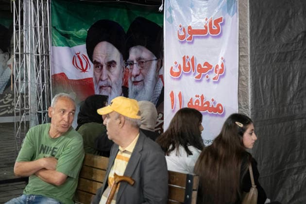 Daily Life In Iran Amid Threat About New Possible War People sit on a sidewalk beneath a banner depicting portraits of Iran s late Supreme Leaders Ayatollah Ruhollah Khomeini and Ayatollah Ali Khamenei in a business district in downtown Tehran, Iran, on May 22, 2026. U.S. President Donald Trump has threatened Iran with the possibility of a new conflict, and according to official reports, he is considering military action if no agreement is reached with Iranian officials. Tehran Tehran Iran  Copyright: xMortezaxNikoubazlx originalFilename: nikoubazl-dailylif260522_npPbO.jpg