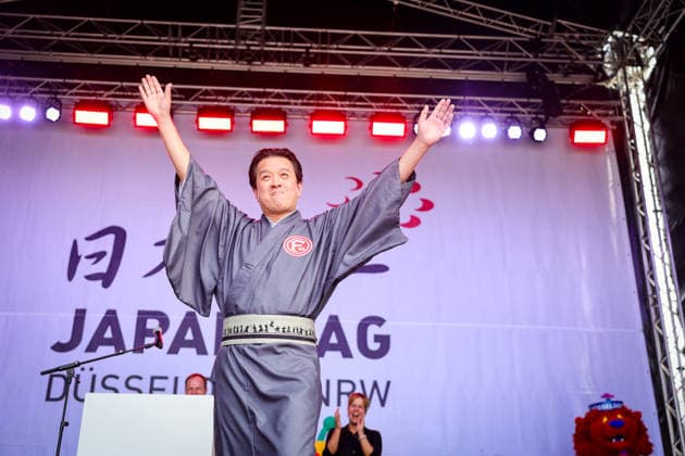 Japan-Tag 2026 in Düsseldorf, einzigartiges Kulturfest in der Landeshauptstadt von NRW - Takao Hariya, Präsident des japanischen Clubs in Düsslddorf bei seienr Begrüssungsrede - im Hitergrund stehen NRW Ministerpräsident Hendrik Wüst, NRW Ministerin für Wirtschaft und Kultur Mona Neubaur und der japanische Generalkonsul für Düsseldorf Yoshitaka Tsunoda überraschte die Zuschauer als bekennender Fan von Fortuna Düsseldorf ... Düsseldorf Burgplatz NRW Deutschland *** Japan Day 2026 in Düsseldorf, unique cultural festival in the state capital of NRW Takao Hariya, President of the Japanese Club in Düsseldorf during his welcoming speech in the background NRW Minister President Hendrik Wüst, NRW Minister for Economics and Culture M