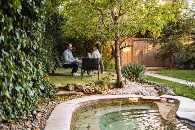 Ein Paar, das sich im Garten hinter dem Haus entspannt und einen Kaffee genießt Couple sitting at a table with drinks in a lush backyard garden with a pond (License=RF) ,model released, Symbolfoto Copyright: xZoonar.com JelenaxCvetkovicx 25051915 ,model released, Symbolfoto ,property released