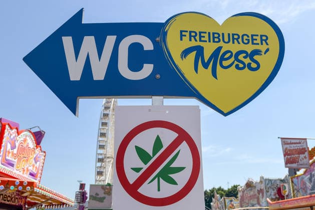 Freiburg im Breisgau GER, Cannabis-Verbot auf Volksfest, Freiburg im Breisgau, 24.05.2026 Wegweiser zur Freiburger Mess und zu den WCs, flankiert von einem Cannabis-Verbotsschild, mit Fahrgeschäften im Hintergrund. *** Freiburg im Breisgau GER, Cannabis ban at folk festival, Freiburg im Breisgau, 24 05 2026 Signpost to the Freiburger Mess and to the WCs, flanked by a cannabis prohibition sign, with rides in the background Copyright: xEibner-Pressefoto ThomasxHessx