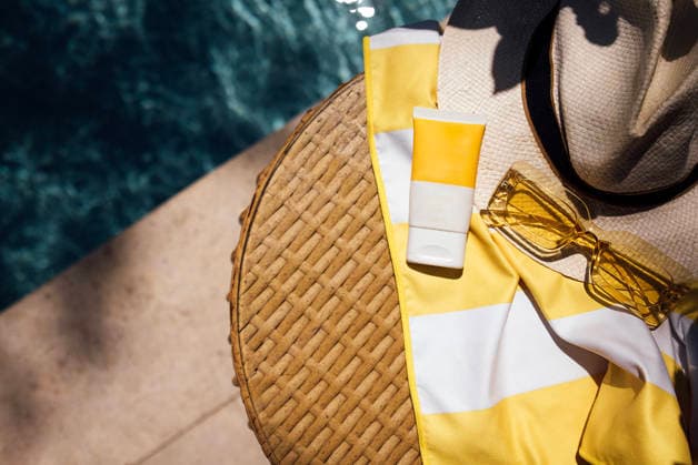 Eine Sommerszene am Pool mit einem Strohhut, einer gelben Sonnenbrille, Sonnencreme und einem gestreiften Strandtuch auf einem geflochtenen Tisch in der Nähe eines glitzernden blauen Pools Poolside arrangement includes a straw hat, yellow sunglasses, sunscreen, and a striped towel on a woven table beside a clear blue swimming pool (License=RF) Copyright: xZoonar.com DashaxPetrenkox 25102896
