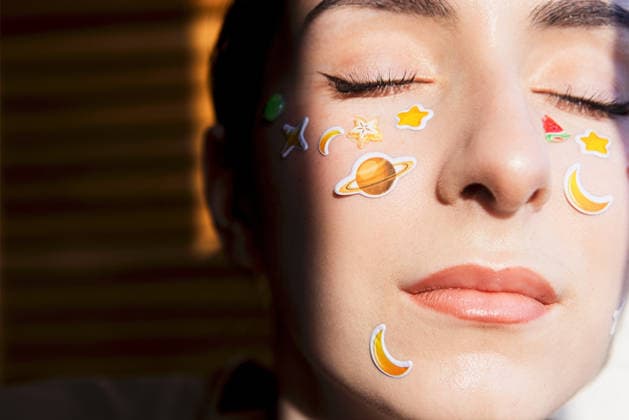 Weibliches Model mit Aufklebern im Gesicht, die Planeten und Sterne darstellen, die Augen geschlossen, von natürlichem Licht beleuchtet, mit einem unscharfen Hintergrund aus horizontalen Linien Woman with decorative stickers on her face, including planets and stars, eyes closed, illuminated by sunlight, with a softly blurred background (License=RF) Copyright: xZoonar.com DashaxPetrenkox 25102980