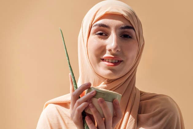Eine junge Frau, die einen leichten Hidschab trägt, hält eine Schale mit einem natürlichen Hautpflegeprodukt und einem Aloe-Vera-Blatt in der Hand und verkörpert Schönheit und Wohlbefinden in einer ruhigen Umgebung Woman in a light hijab is holding a bowl of skincare product with an aloe vera leaf, emphasizing natural beauty and wellness in a calming atmosphere (License=RF) ,model released, Symbolfoto Copyright: xZoonar.com DashaxPetrenkox 25103059 ,model released, Symbolfoto ,property released
