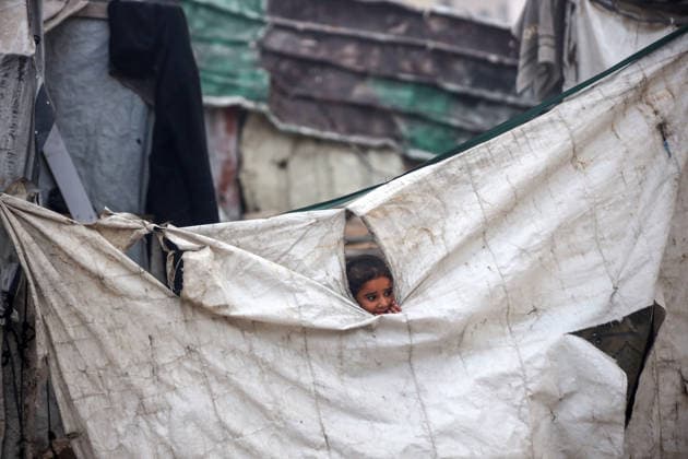 Palestinian Muslims Attend The Eid Al-Adha Prayer, In Gaza City A displaced Palestinian girl peers through a tear in a tent wall as members of Palestinian Islamic Jihad stand on a street during Eid al-Adha in Gaza City, on May 27, 2026. Gaza Palestine  Copyright: xMajdixFathix originalFilename: fathi-notitle260527_npV33.jpg