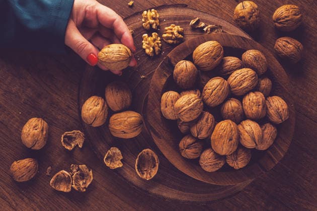 die Hand einer Frau, die einen Walnuss aus einer Holzschale mit Walnüssen nimmt. Es gibt Schalen und Walnüsse, die herum verstreut sind. a woman s hand taking a walnut from a wooden bowl filled with walnuts. There are shells and walnuts scattered around. (License=RF) Copyright: xZoonar.com Galax 25108915