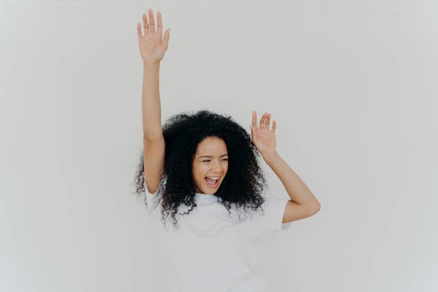 Fröhliche junge Frau mit lockigem Haar, die vor einem weißen Studiohintergrund die Arme hebt und lacht Cheerful Young Woman with Curly Hair Raising Arms and Laughing Against White Studio Background (License=RF) ,model released, Symbolfoto Copyright: xZoonar.com ViorelxKurnosovx 25113006 ,model released, Symbolfoto ,property released