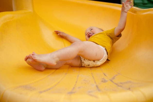 Ein lachendes Kind rutscht auf einer Spielplatzrutsche hinunter Laughing child sliding down yellow playground slide with joyful thrill. Thrilled toddler enjoying fast ride on outdoor play equipment. Happy kid experiencing pure delight during summer playground fun (License=RF) ,model released, Symbolfoto Copyright: xZoonar.com elenaxskorobogatovax 25128023 ,model released, Symbolfoto ,property released
