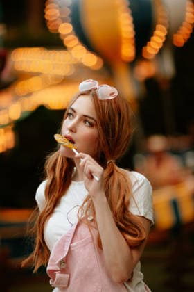 Fair visitor eating a lollipop at an illuminated amusement park model released, Symbolfoto, GMLF01618