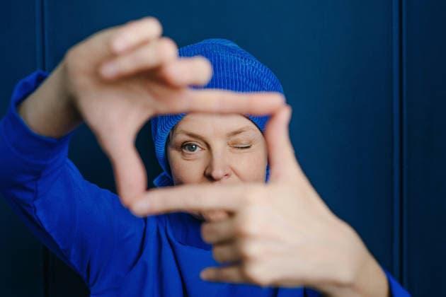 Playful woman in beanie making finger frame on blue wall model released, Symbolfoto property released, YTF04904
