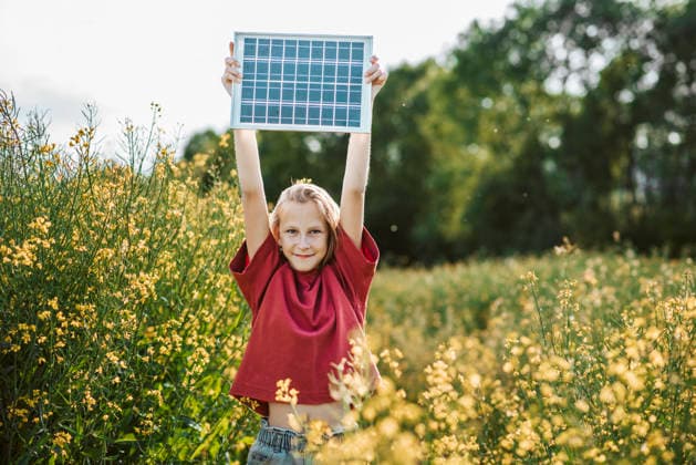 Girl holding solar panel in blooming field with sustainability concept. Young girl holding solar panel outdoors symbolizing renewable energy future. model released