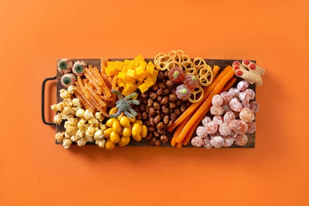 Halloween-Wurst- und Käseplatte mit Kürbis, Schokoladenbonbons, Spinne und Crackern. Halloween sweet charcuterie board with pumpkin, popcorn, dried fruits, color chocolate candy, spider, crackers on orange background. Festive food for kids party. View from above. (License=RF) Copyright: xZoonar.com SvetlanaxLazhkox 25161563