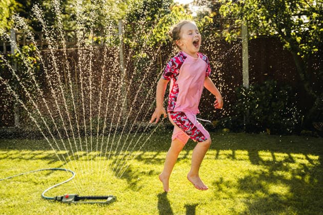 Joyful child running through garden sprinkler in summer backyard Corby, England, United Kingdom CR_ATMT260528-2039573-01 ,model released, Symbolfoto