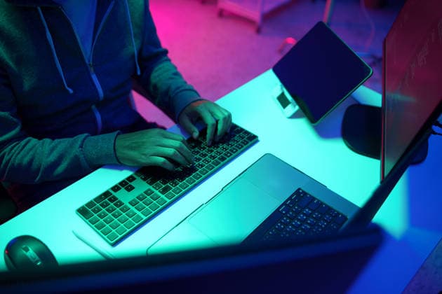 Eine Person, die in einem neonbeleuchteten Computerarbeitsplatz auf einer Tastatur tippt Close-up of a person typing on a keyboard at a modern desk illuminated with vibrant neon blue and pink lighting, creating a moody tech and coding atmosphere (License=RF) ,model released, Symbolfoto Copyright: xZoonar.com SirinarthxMekvorawuthx 25171464 ,model released, Symbolfoto ,property released