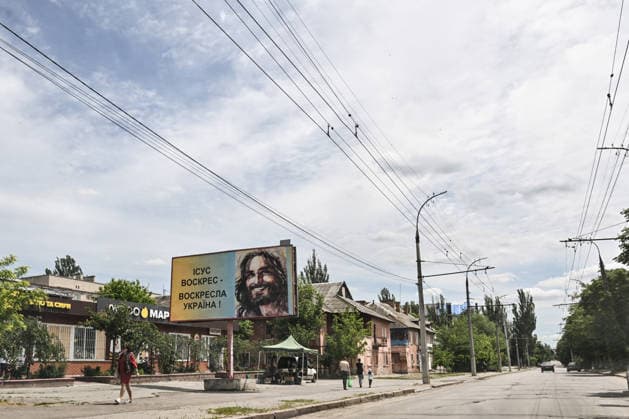 RECORD DATE NOT STATED A billboard reading Jesus is risen — Ukraine will rise again stands on a street in the frontline city of Kherson, Ukraine, on June 2, 2026. The Russian army attacks the city daily with FPV drones and other unmanned aerial vehicles, deliberately terrorizing civilians. Russian forces conduct hunts for local residents, tracking them with FPV drones and dropping explosives. Police officers, medics, public transport, and urban infrastructure are also targeted. Based on the intensity of attacks, Kherson is informally divided into yellow and red zones, with the red zone considered the most dangerous due to constant shelling and drone strikes. Anti-drone netting has been installed above roads to help protect against Russian FPV drone atta  Copyright: xDmytroxSmolienkox