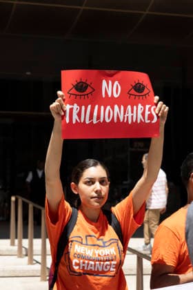 June 12, 2026, New York, New York, USA: A coalition of organizations rally outside JP Morgan Chase headquarters in Midtown Manhattan to disrupt Chase CEO J. Dimon s party celebrating E. Musk s launch of SpaceX s IPO on the Nasdaq Stock Exchange and Musk s net worth as a trillionaire. A protester wears a shirt that reads NEW YORK COMMUNITIES FOR CHANGE and holds a sign that reads NO TRILLIONAIRES. Organizers denounce working people having SpaceX forced into their 401ks and pensions and the emergence of trillionaire-level wealth in the United States while millions of people face housing insecurity, medical debt, and low wages. New York USA  - ZUMAr174 20260612_znp_r174_015 Copyright: xGinaxMxRandazzox