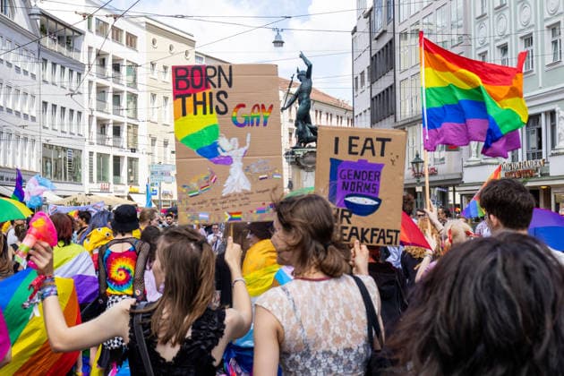Augsburg, Bavaria, Germany June 13, 2026: Participants carrying rainbow flags and wearing colorful costumes take part in Christopher Street Day (CSD) in Augsburg. The parade through the city center promotes the rights of LGBTQ+ people as well as social diversity and tolerance. Participants carrying rainbow flags and signs reading: BORN THIS GAY and I EAT GENDER NORMS *** Teilnehmerinnen und Teilnehmer mit Regenbogenflaggen und bunten Kostümen nehmen am Christopher Street Day (CSD) in Augsburg teil. Der Demonstrationszug durch die Innenstadt wirbt für die Rechte von LGBTQ+-Menschen sowie für gesellschaftliche Vielfalt und Toleranz. Teilnehmer mit Regenbogenfahnen und Flaggen und Schildern mit Aufschrift: BORN THIS GAY und I EAT GENDER