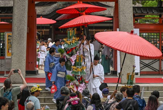 Osaka Keeps Centuries Old Otaue Rice Festival alive OSAKA, JAPAN - JUNE 14: Attendants hold large red umbrellas (nagae no kasa) to shade Ueme rice-planting maidens carrying blessed rice seedlings as they exit the main pavilion gate during the historic Otaue Rice Planting Festival (Otaue Shinji) at Sumiyoshi Taisha Shrine in southern Osaka, Japan, on June 14, 2026. The ancient agricultural ritual, officially designated as an Important Intangible Folk Cultural Property of Japan, features these selected maidens transporting the consecrated seedlings from the inner sanctuary down to the holy paddy field under ritual escort to pray for a bountiful harvest. Artur Widak Anadolu Agency Anadolu Osaka Japan. Editorial use only. Please get in touc  Copyright: x2026xAnadoluxArturxWidak AnadoluxAgencyx
