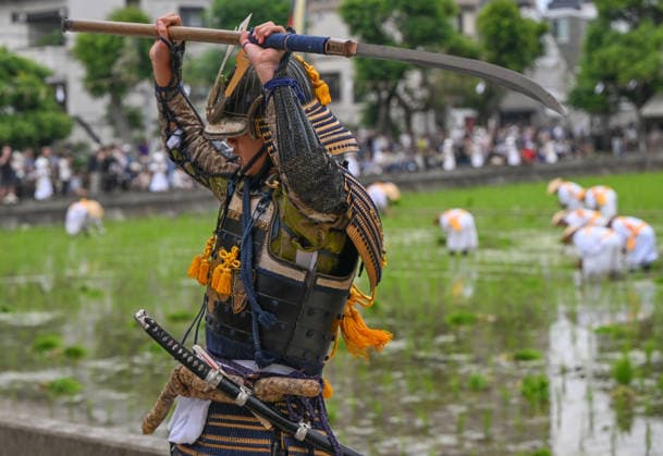 Osaka keeps centuries old Otaue Rice Festival alive OSAKA, JAPAN - JUNE 14: A performer dressed as a Furyu-musha samurai warrior brandishes a traditional long-bladed polearm (naginata) over his head while field workers plant seedlings in the background during the historic Otaue Rice Planting Festival (Otaue Shinji) at Sumiyoshi Taisha Shrine in southern Osaka, Japan, on June 14, 2026. The ancient agricultural ritual, officially designated as an Important Intangible Folk Cultural Property of Japan, features these stylized martial arts performances around the banks of the sacred paddy field to ward off evil spirits and protect the new crop. Artur Widak Anadolu Osaka Japan. Editorial use only. Please get in touch for any other usage.  Copyright: x2026xAnadoluxArturxWidakx