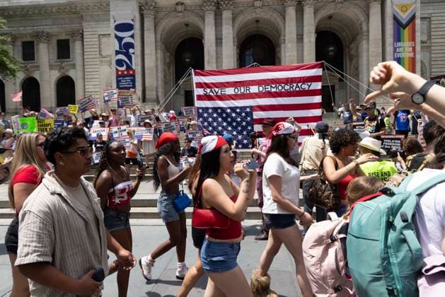 June 14, 2026, New York, New York, USA: People pass by demonstrators at Rise and Resist s We Are In A State Of Emergency Flag Day anti-Trump protest on the steps of the New York Public Library (NYPL) branch on Fifth Avenue in Midtown Manhattan where a giant upside down flag is hoisted reading SAVE OUR DEMOCRACY. New York USA  - ZUMAr174 20260614_znp_r174_020 Copyright: xGinaxMxRandazzox