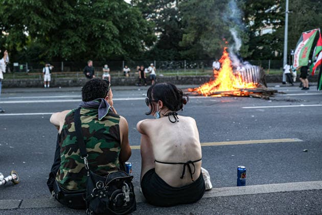 June 14, 2026, Geneva, Switzerland, European Union: A couple watches from behind as a fire burns from debris in the street during demonstrations in Geneva ahead of the G7 summit, which begins tomorrow in Evian-les-Bains. Geneva European Union - ZUMAo116 20260614_znp_o116_028 Copyright: xBiancaxOterox