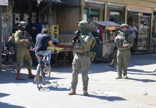 Palestinian-Israeli conflict in Nablus, Palestine - 18 Jun 2026 A Palestinian rides his bicycle past soldiers stationed at the entrance to the market during a raid on Balata refugee camp, east of Nablus in the West Bank. Israeli forces raided the central market during a security operation. Palestinian sources said that the army arrested seven Palestinians from various neighborhoods in Nablus and its surrounding refugee camps. Nablus Palestine Copyright: xNasserxishatyehx xSOPAxImagesx Nishtayeh2330