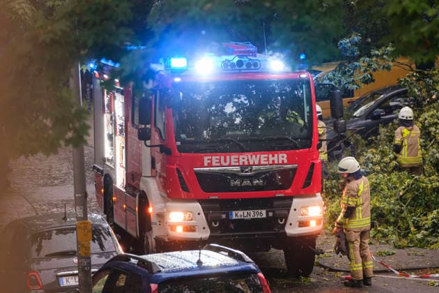 Ein Löschfahrzeug der Feuerwehr Köln mit eingeschaltetem Blaulicht im nächtlichen Dauereinsatz in Köln-Nippes; Einsatzkräfte beseitigen nach einem schweren Unwetter mit Sturmböen und Gewittern umgestürzte Bäume und blockierte Straßen im Kölner Stadtgebiet. *** A Cologne fire department truck with flashing blue lights during a continuous emergency operation in Cologne-Nippes; firefighters clearing fallen trees and blocked roads after a severe storm with heavy thunderstorms and gales. Nordrhein-Westfalen Deutschland, Germany DSCF6995