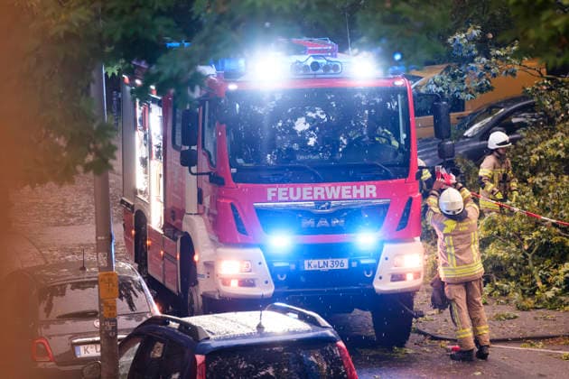 Ein Löschfahrzeug der Feuerwehr Köln mit eingeschaltetem Blaulicht im nächtlichen Dauereinsatz in Köln-Nippes; Einsatzkräfte beseitigen nach einem schweren Unwetter mit Sturmböen und Gewittern umgestürzte Bäume und blockierte Straßen im Kölner Stadtgebiet. *** A Cologne fire department truck with flashing blue lights during a continuous emergency operation in Cologne-Nippes; firefighters clearing fallen trees and blocked roads after a severe storm with heavy thunderstorms and gales. Nordrhein-Westfalen Deutschland, Germany DSCF6999