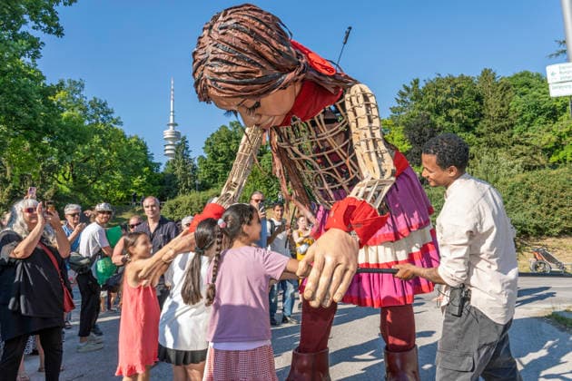 News Bilder des Tages Eröffnung des Tollwood Sommerfestivals 2026, Little Amal begleitet die Festival-Eröffnung, die berühmte 3,5 Meter große Puppe, die das zehnjährige syrische Flüchtlingsmädchen Amal verkörpert, wurde weltweit zu einem Sinnbild für Hoffnung un Deutschland, München, 19. Juni 2026, Eröffnung des Tollwood Sommerfestivals 2026, Little Amal begleitet die Festival-Eröffnung, die berühmte 3,5 Meter große Puppe, die das zehnjährige syrische Flüchtlingsmädchen Amal verkörpert, wurde weltweit zu einem Sinnbild für Hoffnung und Menschlichkeit, Kinder überreichen ihr zur Begrüßung selbstgebasteltete Geschenke, im Hintergrund der Olympiaturm, das Tollwood ist ein multikulturelles Festival, das im Sommer im Olympiapark stat