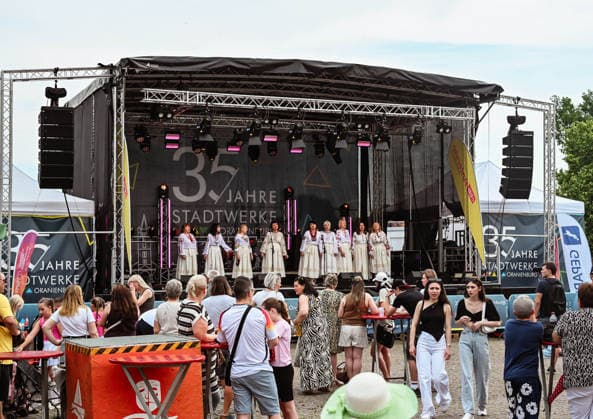 20.06.2026, xlakx, Entertainment, Oranienburger Stadtfest v.l. Besucher verfolgen einen Bühnenauftritt beim Stadtfest Oranienburg. Eine Gesangsgruppe in traditionellen Trachten tritt auf der Hauptbühne vor dem Jubiläumsbanner 35 Jahre Stadtwerke Oranienburg auf Oranienburg *** June 20, 2026, xlakx, Entertainment, Oranienburg City Festival v l Visitors watch a stage performance at the Oranienburg City Festival A singing group in traditional costumes performs on the main stage in front of the banner celebrating the 35th anniversary of Stadtwerke Oranienburg Oranienburg,detected_source_language Daniel Lakomski