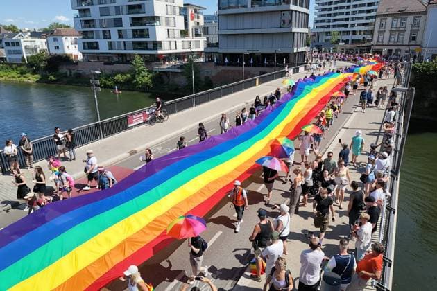 Teilnehmende tragen beim Christopher Street Day (CSD) eine ueber 100 Meter lange und 4,2 Meter breite Regenbogenfahne ueber die Herdbruecke, die das in Baden-Wuerttemberg gelegenen Ulm mit dem in Bayern gelegenen Neu-Ulm verbindet (Foto vom 20.06.2026). Die Veranstalter bezeichnen sie als die groesste Regenbogenfahne Deutschlands. Der CSD steht in diesem Jahr unter dem Motto Von Ufer zu Ufer: Wir halten zusammen! und findet zum 15. Mal statt. EDITORIAL USE ONLY *** During Christopher Street Day (CSD), participants carry a rainbow flag over 100 meters long and 4.2 meters wide across the Herdbruecke, which connects Ulm, located in Baden-Württemberg, with Neu Ulm, located in Bavaria. Photo from June 20, 2026. The organizers describe it as th Copyright: epd-bild ThomasxHeckmann 5 - Kopieren
