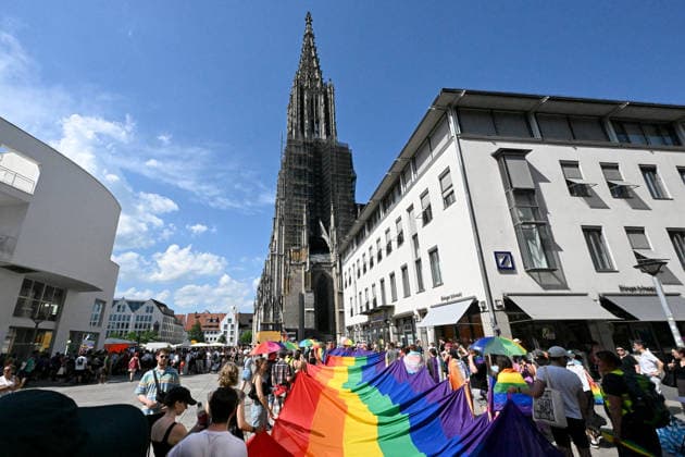 Teilnehmende tragen beim Christopher Street Day (CSD) in Ulm und Neu-Ulm eine ueber 100 Meter lange und 4,2 Meter breite Regenbogenfahne (Foto vom 20.06.2026). Die Veranstalter bezeichnen sie als die groesste Regenbogenfahne Deutschlands. Der CSD steht in diesem Jahr unter dem Motto Von Ufer zu Ufer: Wir halten zusammen! und findet zum 15. Mal statt. EDITORIAL USE ONLY *** Participants at Christopher Street Day (CSD) in Ulm and Neu Ulm are carrying a rainbow flag over 100 meters long and 4.2-meter-wide rainbow flag. Photo taken on June 20, 2026. The organizers describe it as Germany’s largest rainbow flag. This year’s CSD is themed From Shore to Shore Copyright: epd-bild ThomasxHeckmann 260620_Heckmann_Ulm_CSD_Regenbogenfahne_2397