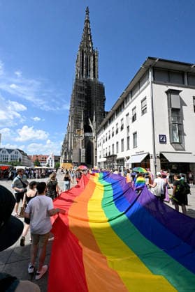 Teilnehmende tragen beim Christopher Street Day (CSD) in Ulm und Neu-Ulm eine ueber 100 Meter lange und 4,2 Meter breite Regenbogenfahne (Foto vom 20.06.2026). Die Veranstalter bezeichnen sie als die groesste Regenbogenfahne Deutschlands. Der CSD steht in diesem Jahr unter dem Motto Von Ufer zu Ufer: Wir halten zusammen! und findet zum 15. Mal statt. EDITORIAL USE ONLY *** Participants at Christopher Street Day (CSD) in Ulm and Neu Ulm are carrying a rainbow flag over 100 meters long and 4.2-meter-wide rainbow flag. Photo taken on June 20, 2026. The organizers describe it as Germany’s largest rainbow flag. This year’s CSD is themed From Shore to Shore Copyright: epd-bild ThomasxHeckmann epd-Regenbogenfahne6 - Kopieren