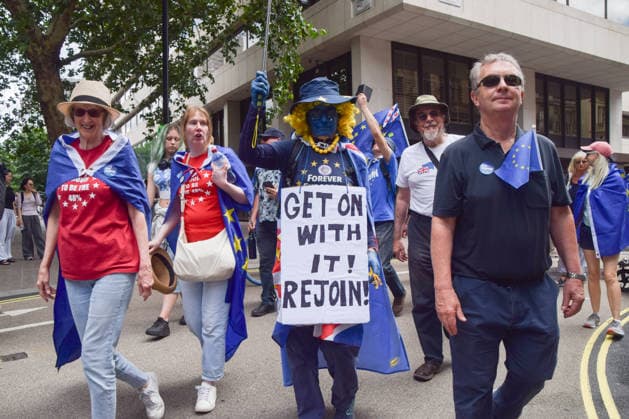 National Rejoin March on the tenth anniversary of the Brexit referendum in London, UK - 20 Jun 2026 A protester wears makeup in the colours of the EU flag and carries a placard stating Get on with it, rejoin during the National Rejoin March, calling on the UK government to rejoin the European Union on the tenth anniversary of the Brexit referendum. London United Kingdom Copyright: xVukxValcicx xSOPAxImagesx VukValcicNationalRejoinMarch200626_49