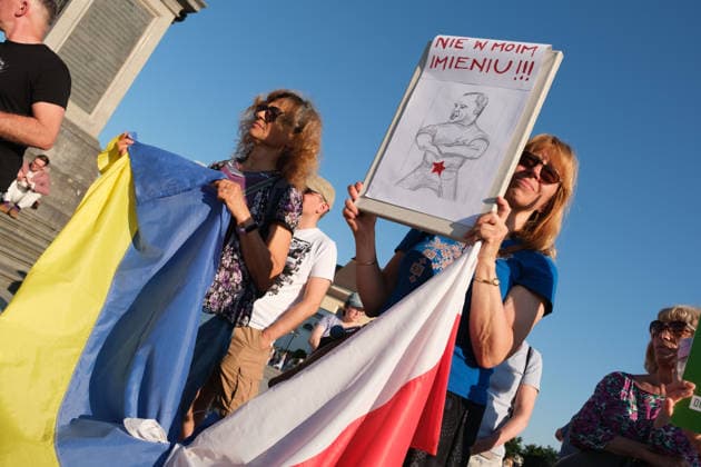 June 20, 2026, Warsaw, Masovian Voivodeship, Poland: Protesters hold a Polish and Ukrainian flag tied together during a demonstration on Warsaw s Castle Square for World Refugee Day. Organized under the slogan open republic, the rally was held in protest against growing xenophobia towards migrants and refugees in Poland, as well as the increasing use of anti-migrant rhetoric by Polish conservatives and far-right politicians. The protester on the right holds up a placard with a caricature of Polish President Karol Nawrocki and the words not in my name! Warsaw Poland - ZUMAk204 20260620_zip_k204_037 Copyright: xRomanxKozielx