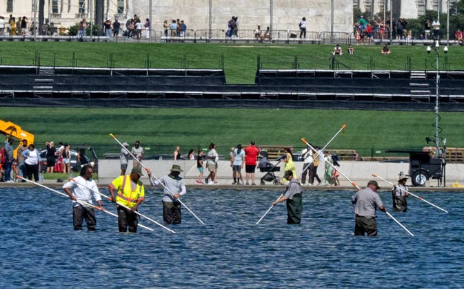 National Park Service workers use vacuum pumps to clean algae off the bottom of the newly renovated Lincoln Memorial Reflecting Pool on the National Mall in Washington, DC on Saturday, June 20,2026. The Trump Administration awarded no-bid contracts totaling nearly $15 million to renovated Reflecting Pool but it is now filled with algae and the paint is peeling. Dozens of National Guard and other police stop people from taking the blue paint chips floating in the water, with some arrests.  WAP2026062010 PATxBENIC