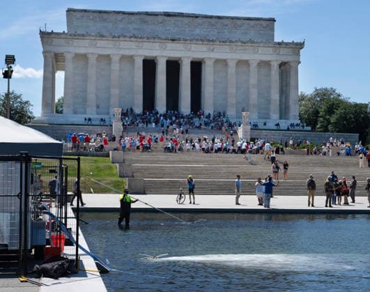 Hydrogen Peroxide is pumped into the newly renovated Lincoln Memorial Reflecting Pool to clean algae as residents and tourists walk by on the National Mall in Washington, DC on Saturday, June 20,2026. The Trump Administration awarded no-bid contracts totaling nearly $15 million to renovated Reflecting Pool but it is now filled with algae and the paint is peeling. Dozens of National Guard and other police stop people from taking the blue paint chips floating in the water, with some arrests.  WAP2026062017 PATxBENIC