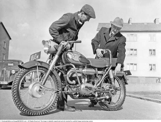Monark Blue Arrow 1954. Die beiden Männer betrachten den Aufbau des neuen Motorrads und weisen auf ein bestimmtes Detail hin: das Stützpedal für den Beifahrer, das damals eine Neuheit darstellte. Die Monark Blue Arrow: Eine skandinavische Ikone der 1950er Jahre – die Monark Blue Arrow (M550), das schwedische Kraftpaket, das 1954 die International Six Days Trial im Sturm eroberte und acht Goldmedaillen holte.Angetrieben von einem 250 ccm JLO Zweizylinder Zweitaktmotor verband diese Maschine minimalistisches nordisches Design mit robuster Zuverlässigkeit Ursprünglich für den Sport gebaut, führte ihre Leistungsfähigkeit zu einem Großauftrag der schwedischen Streitkräfte und festigte damit ihren Status als Legende jener Zeit Monark Blue A Copyright: imageBROKER Sjoberg ibljsj18095897.jpg