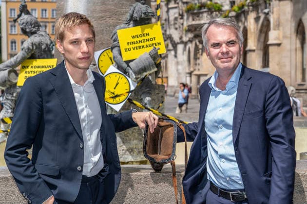 Oberbürgermeister Dominik Krause, Die Grünen, und Stadtkämmerer Christoph Frey, (rechts), zeigen am Fischbrunnen symbolisch die leere Stadtkasse her, beim bundesweiten Aktionstag Kommunalfinanzen, Münchner Aktion 5 vor 12, München, 22. Juni 2026 Deutschland, München, 22. Juni 2026, Oberbürgermeister Dominik Krause, Die Grünen, und Stadtkämmerer Christoph Frey, (rechts), zeigen am Fischbrunnen symbolisch die leere Stadtkasse her, beim bundesweiten Aktionstag Kommunalfinanzen, Münchner Aktion 5 vor 12, wollen damit auf die dramatische kommunale Finanzsituation aufmerksam machen, Finanzlage der Städte, Landkreise und Gemeinden ist dramatisch, hohe Defizite und Schulden in den Haushalten, der Aktionstag wird vom Deutschen Städtetag,