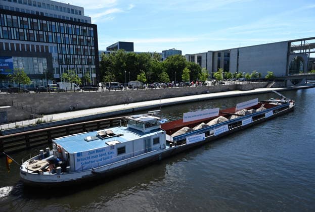 Cargo ship blocks Spree River during rally in Berlin BERLIN, GERMANY - JUNE 24: Participants gather on the banks of the Spree River as a cargo ship blocks the waterway in front of the Reichstag building during a rally organized by MIRO, the German minerals and aggregates industry association, in Berlin, Germany, on June 24, 2026. An 80-meter cargo ship loaded with construction aggregates blocked traffic on the Spree River while demonstrators called for stronger legal protection of mineral deposits and greater consideration of domestic mineral resource extraction and processing in spatial planning legislation. Volodymyr Sindieiev Anadolu Berlin Germany. Editorial use only. Please get in touch for any other usage.  Copyright: x2026xAnadoluxVolodymyrxSindieievx