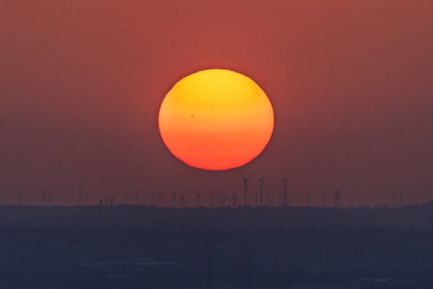 Sonnenuntergang in der Bonn Windräder eines Windparks zeichnen sich als Silhouette vor der riesigen glutroten Sonnenscheibe ab. Auf der Sonne sind Sonnenflecken zu erkennen. Der Hitze-Dunst nach einem Hitzetag mit bis zu 35 Grad lässt die Sonne beim Sonnenuntergang über dem Bonner Raum überdimensional groß erscheinen. Blick vom Petersberg im Siebengebirge. Königswinter Petersberg Nordrhein-Westfalen Deutschland *** Sunset in Bonn: The wind turbines of a wind farm stand out as a silhouette against the huge, glowing-red disk of the sun. Sunspots are visible on the sun. The heat haze following a hot day with temperatures reaching up to 35 degrees makes the sun appear enormous as it sets over the Bonn area. View from Petersberg in the Sie Copyright: xMarcxJohnx