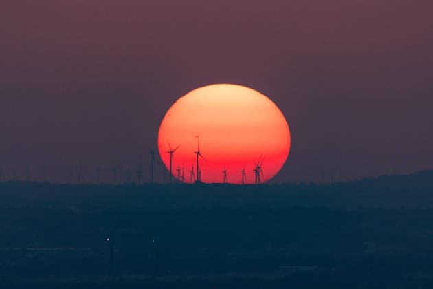 Sonnenuntergang in der Bonn Windräder eines Windparks zeichnen sich als Silhouette vor der riesigen glutroten Sonnenscheibe ab. Auf der Sonne sind Sonnenflecken zu erkennen. Der Hitze-Dunst nach einem Hitzetag mit bis zu 35 Grad lässt die Sonne beim Sonnenuntergang über dem Bonner Raum überdimensional groß erscheinen. Blick vom Petersberg im Siebengebirge. Königswinter Petersberg Nordrhein-Westfalen Deutschland *** Sunset in Bonn: The wind turbines of a wind farm stand out as a silhouette against the huge, glowing-red disk of the sun. Sunspots are visible on the sun. The heat haze following a hot day with temperatures reaching up to 35 degrees makes the sun appear enormous as it sets over the Bonn area. View from Petersberg in the Sie Copyright: xMarcxJohnx