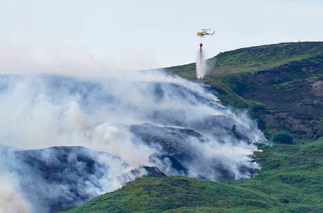June 25, 2026, Glossop, Derbyshire, UK: Glossop, UK. A helicopter throws water above a wildfire as burns near a forest in Glossop near Wood Head Reservoir, Derbyshire. A four-day amber heat and extreme heat warning has been put in place by the Met Office, with temperatures expected to peak by the end of the week. Glossop UK  - ZUMAl94_ 20260625_zaf_l94_046 Copyright: xIoannisxAlexopoulosx