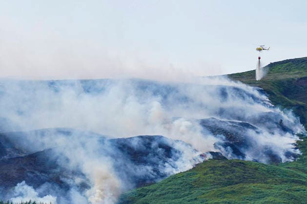 June 25, 2026, Glossop, Derbyshire, UK: Glossop, UK. A helicopter throws water above a wildfire as burns near a forest in Glossop near Wood Head Reservoir, Derbyshire. A four-day amber heat and extreme heat warning has been put in place by the Met Office, with temperatures expected to peak by the end of the week. Glossop UK  - ZUMAl94_ 20260625_zaf_l94_048 Copyright: xIoannisxAlexopoulosx